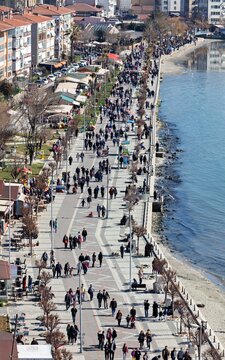 Aerial view of a crowded seaside promenade with pedestrians walking along the paved walkway, cafes, and the calm sea in Istanbul, Turkey.