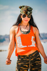 Woman in camouflage and orange tank top stands confidently by water © ExploringandLiving