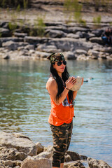 Woman stands by river, holding stone © ExploringandLiving