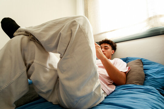 Teen Rests on Blue Bed While Using a Smartphone 