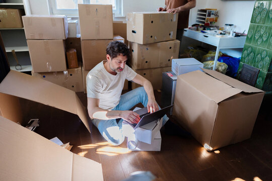 Man Using Laptop During Move Surrounded By Boxes