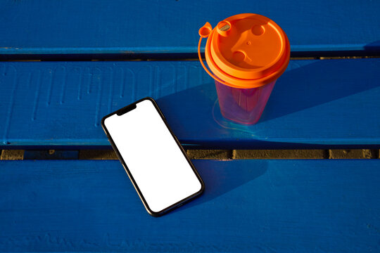 Smartphone Mockup and Reusable Coffee Cup on Blue Bench in Sunlight