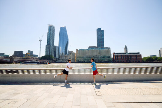Two men engage in a warm-up routine by the banks of the Thames 