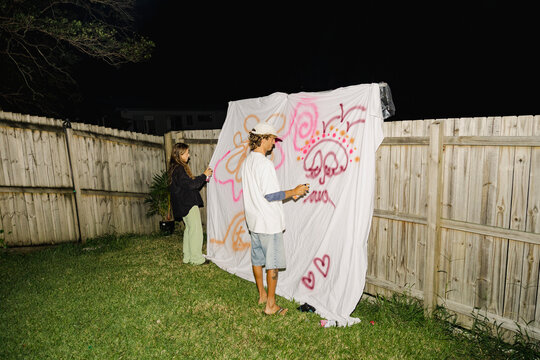 Friends painting graffiti sheet at backyard night party