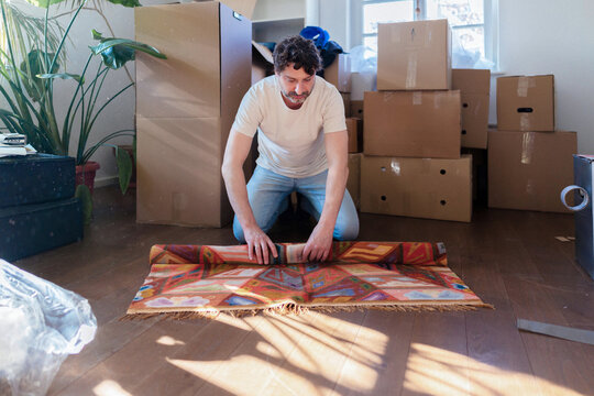 Man Unpacking Rug in New Home Surrounded by Boxes