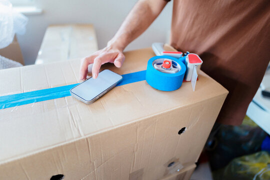 Person Packing Cardboard Boxes With Phone And Tape