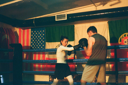Female boxer punches coach with mitt pads in gym