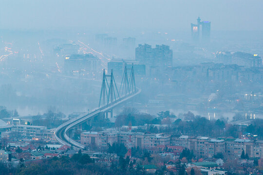 Aerial view of Ada Bridge spanning the Sava River amidst a thick winter fog over the urban skyline of Belgrade, Serbia.