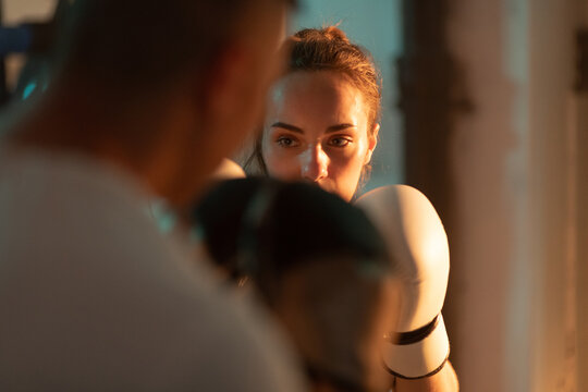 Female boxer exercises with man trainer in boxing gym