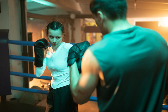 Woman boxer fights man coach with mitt pads in boxing gym