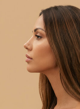 Side profile view of attractive young woman with straight long hair on beige background.