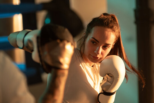Woman boxer hits trainer with mitt pads with right hook in boxing gym.