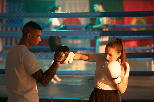 Woman boxer attacks trainer with mitt pads near boxing ring in the gym