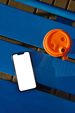 Smartphone Mockup and Reusable Coffee Cup on Blue Bench in Sunlight