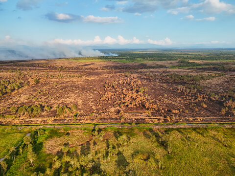 Aerial view of burnt vegetation and smoke from a forest fire across the landscape with green patches and a road in the foreground in Banjarbaru, South Kalimantan, Indonesia.