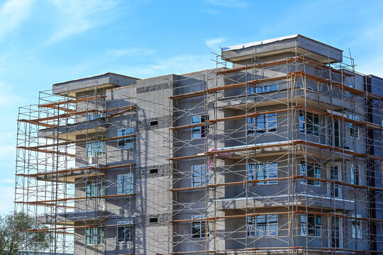 Multistory apartment building under construction with exterior scaffolding, illustrating multifamily housing development, residential construction, urban growth, and real estate investment
