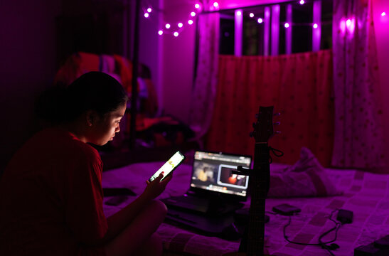 Indian young woman browsing internet in smartphone at night inside 