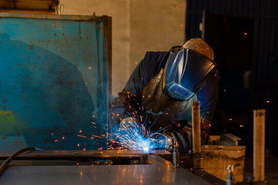 Industrial welder welding steel with bright sparks in manufacturing workshop