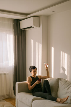 A woman turns on the air conditioner while looking at her phone 