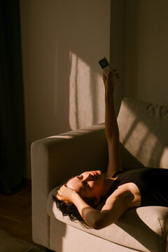 Person Relaxing on a Couch While Holding a AC Remote Control