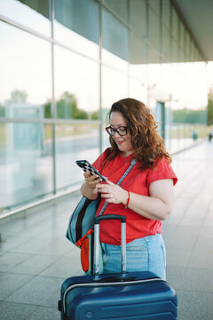 Woman using smartphone with suitcase at airport 
