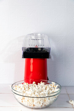 Red air popcorn popper, popping popcorn into a clear glass bowl in a white tile surface 