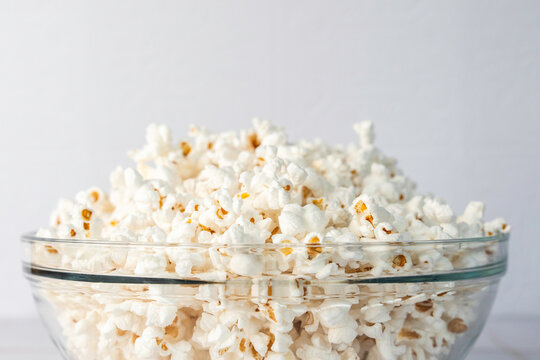 Popcorn in a clear glass bowl on a white tile surface 