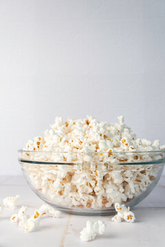 Popcorn in a clear glass bowl on a white tile surface 