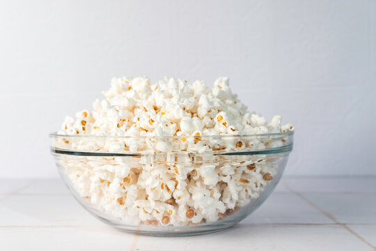 Popcorn in a clear glass bowl on a white tile surface 