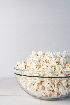 Popcorn in a clear glass bowl on a white tile surface 