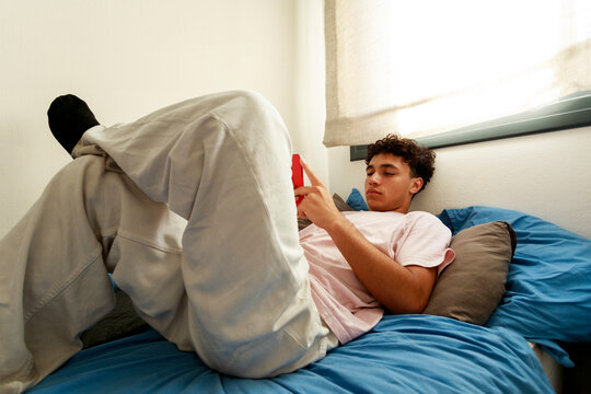 Teenager Relaxes on a Bed While Using a Smartphone 