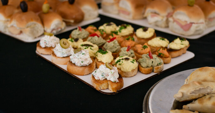 Mesa de bocadillos salados para recepci&oacute;n. Bandeja de canap&eacute;s cremosos, mini s&aacute;ndwiches de jam&oacute;n y queso, y empanadas. Catering para eventos.