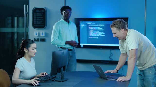 Diverse team of creative software developers collaborating on coding project, presenting programming algorithm script on screen in modern tech startup office workplace environment with neon lighting.