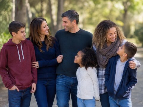 Patchworkfamilie im Park &ndash; Erwachsene und Kinder gehen entspannt nebeneinander, l&auml;cheln sich an und zeigen Zusammenhalt, Zugeh&ouml;rigkeit, Vielfalt und echte famili&auml;re N&auml;he.