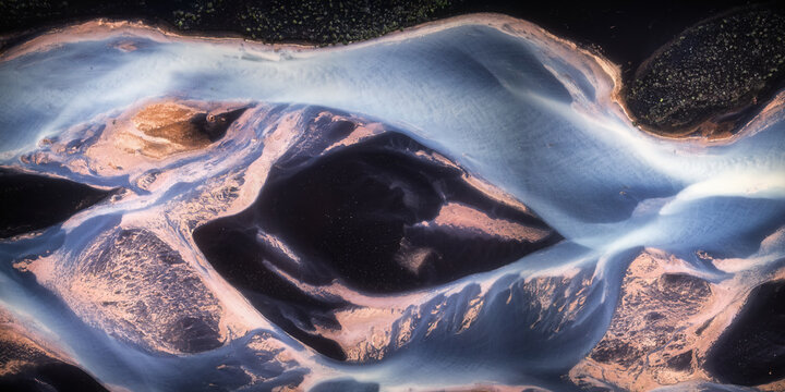 Aerial view of a braided glacial river system with dark volcanic sand and light blue water in the Southern Region, Iceland.