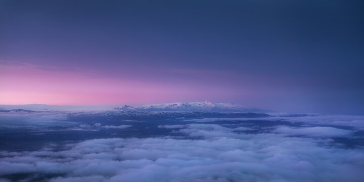 Aerial view of Laki volcanic region with snow-capped mountains rising above a sea of clouds under a vibrant purple sunset sky in Skaftarhreppur, Iceland.