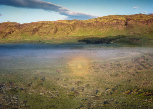 Aerial view of a sun halo glowing over the misty valley of Laugaras, with lush green hills and golden hour light illuminating the Icelandic landscape in Laugaras, Blaskogabyggd, Iceland.