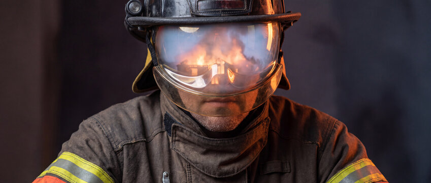 Firefighter in helmet with flames reflected on visor wearing protective turnout gear