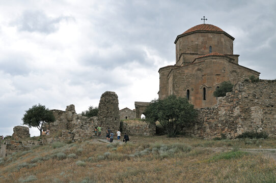 Ancient stone Jvari Monastery with medieval stone ruins and visitors walking along the hill path under an overcast sky in Mtskheta, Georgia