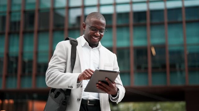 Black businessman, using tablet, browsing report, outdoor near office building. African american business man smiling, works as marketing director, staying connected with technology, leading projects.