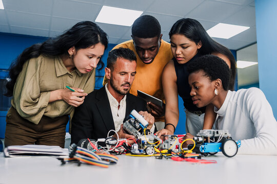 Diverse group of young university students and hispanic teacher working on a robotics project and cars in classroom. Multicultural latin people in technology class in Latin America