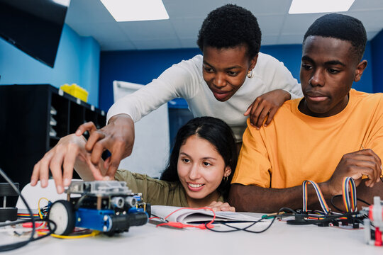 Diverse group of young university students and hispanic teacher working on a robotics project and cars in classroom. Multicultural latin people in technology class in Latin America