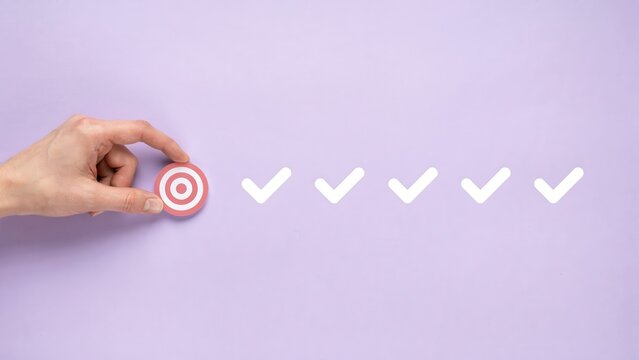 Hand placing a target icon next to a row of checkmarks, symbolizing successful goal achievement, strategic business planning, task completion, and project management objectives on a pastel background