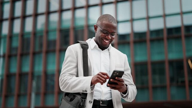 Black businessman, using smartphone, messaging client, outdoor near office building. African american business man smiling, works as startup founder, prepared for client meeting, managing accounts.