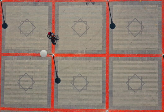 Aerial view of a person riding a bicycle across a paved square with geometric star patterns and vibrant red grid lines in Konya, Konya, Turkiye.