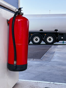  Safety equipment at gas station with fuel tanker behind. Fire extinguisher on service station wall.