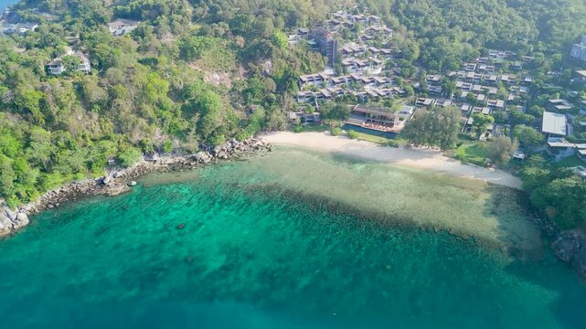 Tropical island landscape in Phuket features green mountains, luxury resorts along the beach, and boats resting in calm blue ocean water near coral reefs