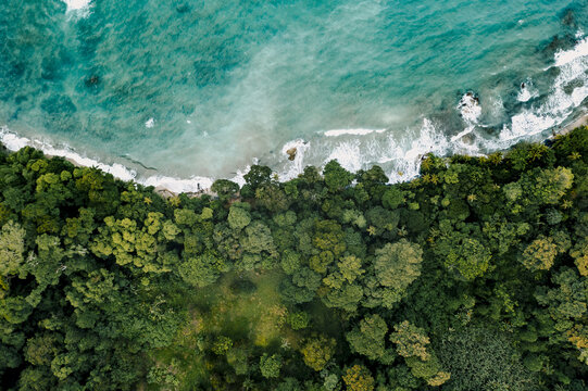Aerial view of the lush tropical forest meeting the turquoise Caribbean sea with waves crashing against the coastline in Puerto Viejo de Talamanca, Limon Province, Costa Rica.