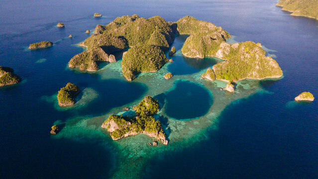 Aerial view of Raja Ampat Islands featuring lush green karst islets surrounded by turquoise coral reefs and deep blue ocean waters in Waigeo Barat, Southwest Papua, Indonesia.