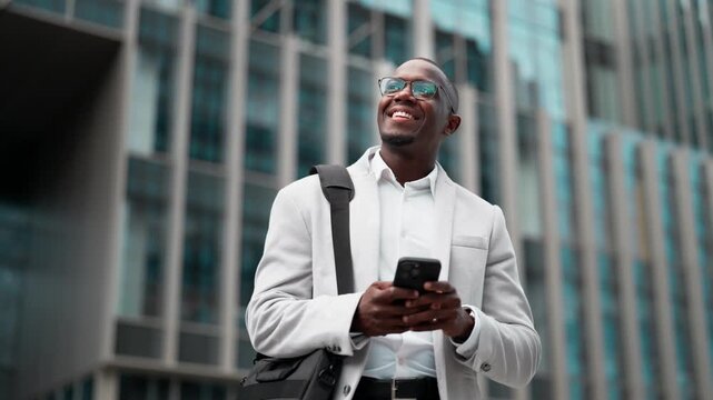 Black businessman, using smartphone, calling, outdoor near office building. African american business man smiling, works as entrepreneur, staying connected with technology, managing accounts.
